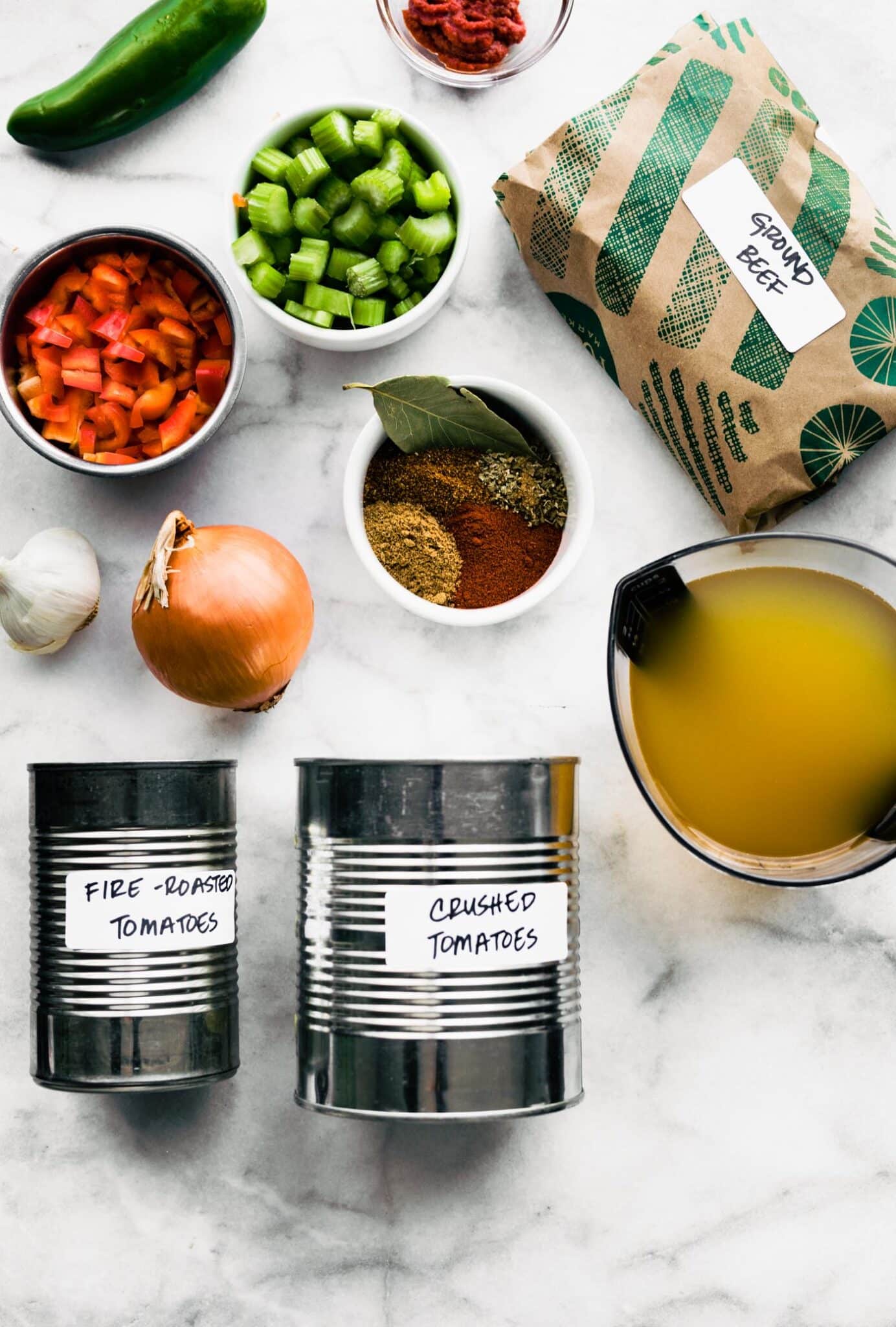 Ingredients for slow cooker beef chili without beans on a white marble countertop.