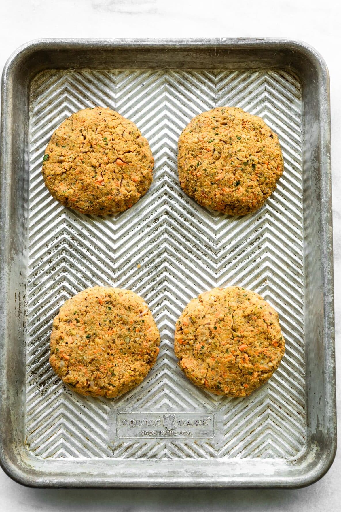 Four unbaked veggie burgers on a metal sheet pan.