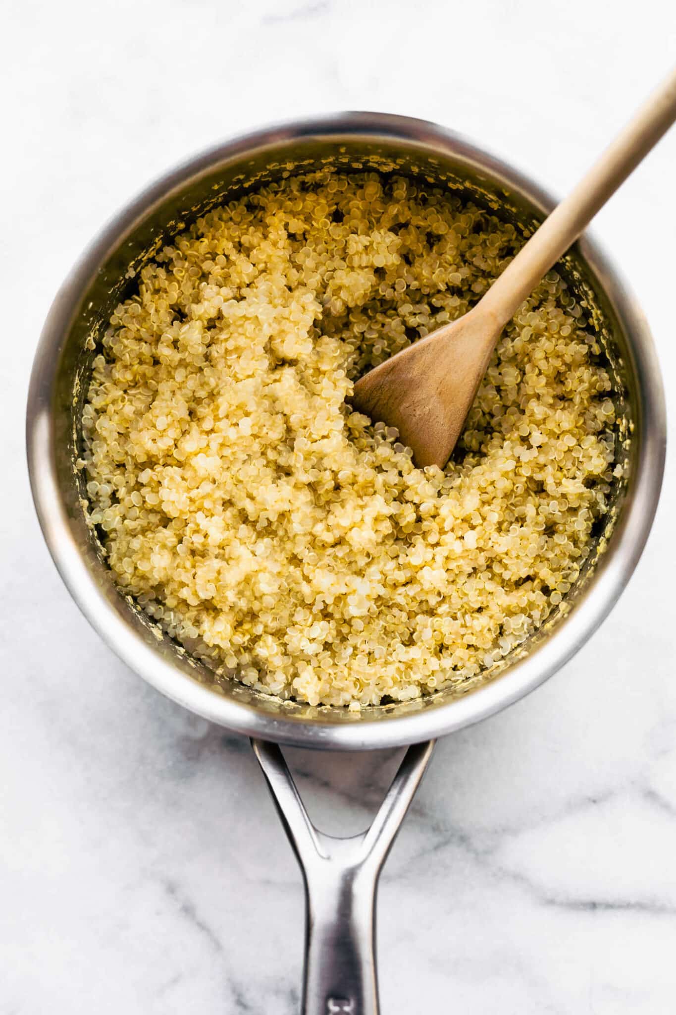 Cooked quinoa in a metal soup pot with a wooden spoon.
