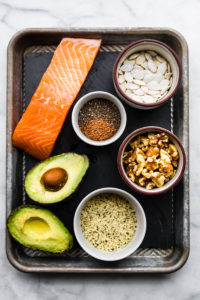 various fat sources including salmon, avocado, and walnuts on a baking sheet