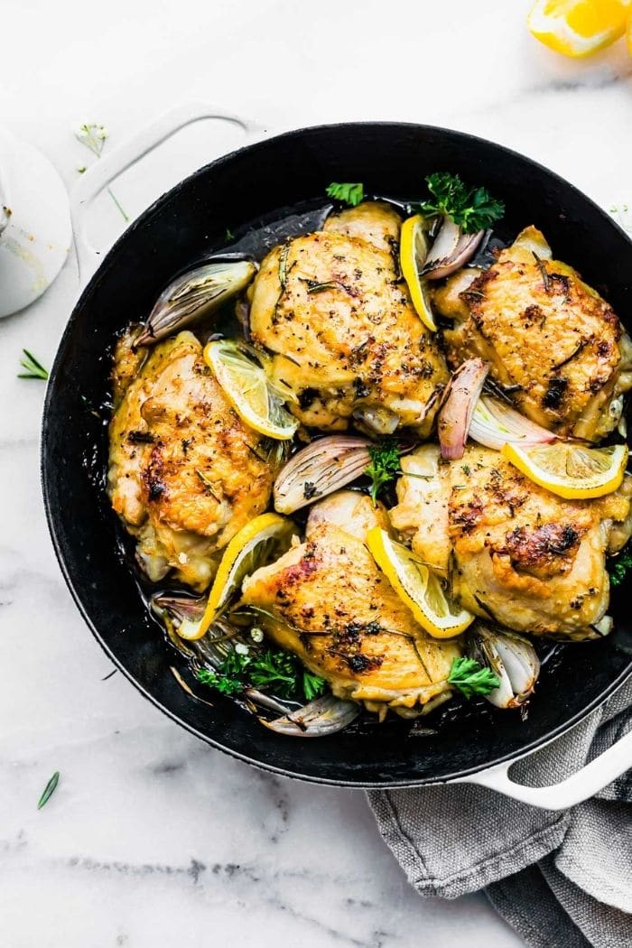 bone-in chicken thighs with crispy skin in skillet with lemon slices and onions