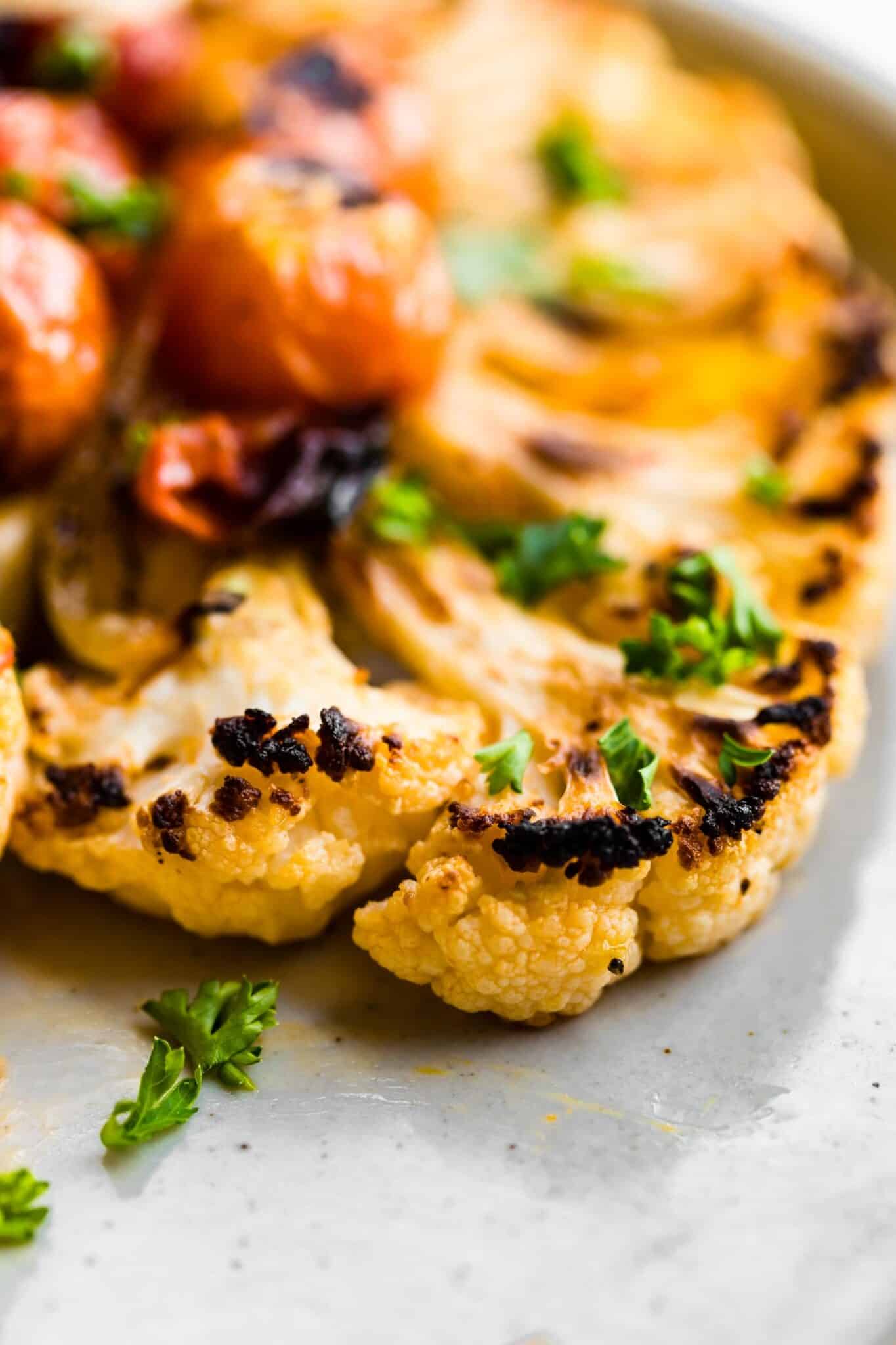 Up close side photo of a charred cauliflower steak with fresh herbs.