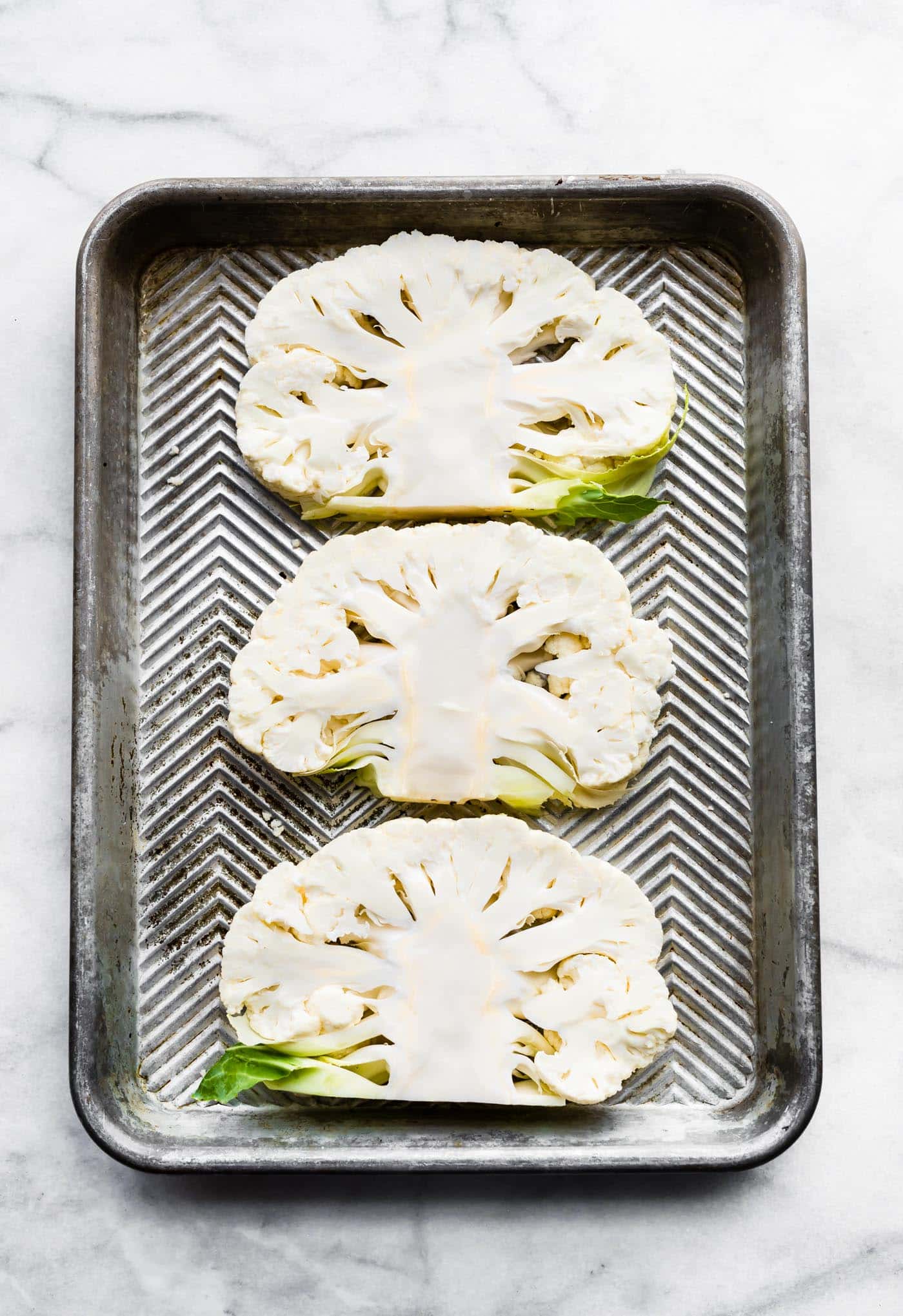 Three raw cauliflower steaks on a sheet pan.