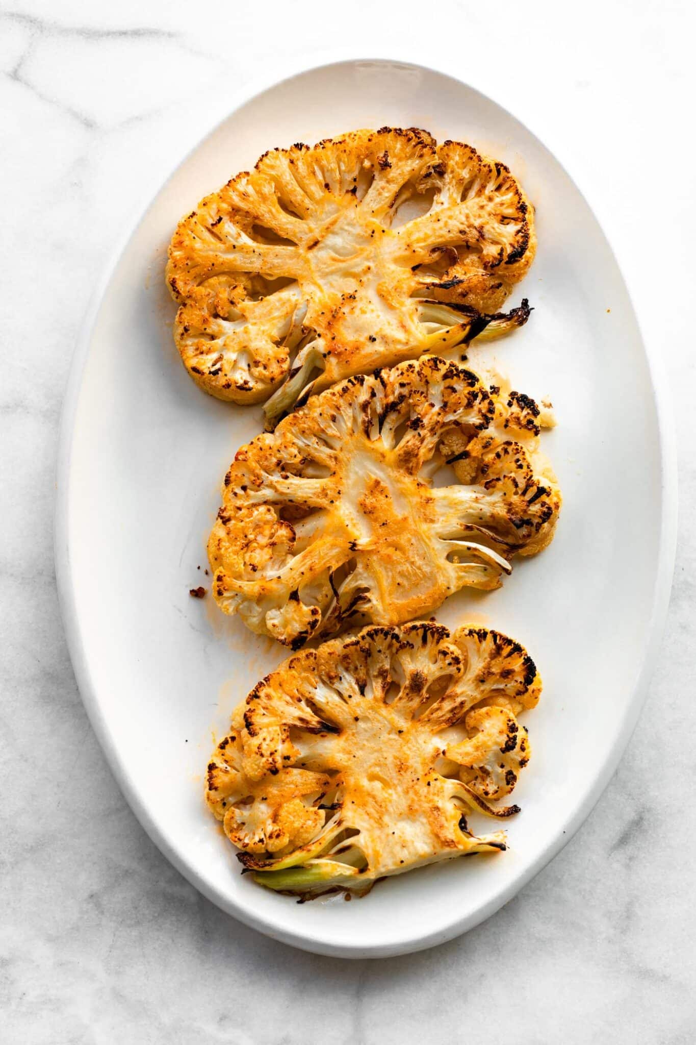 Three roasted cauliflower steaks on a white plate.