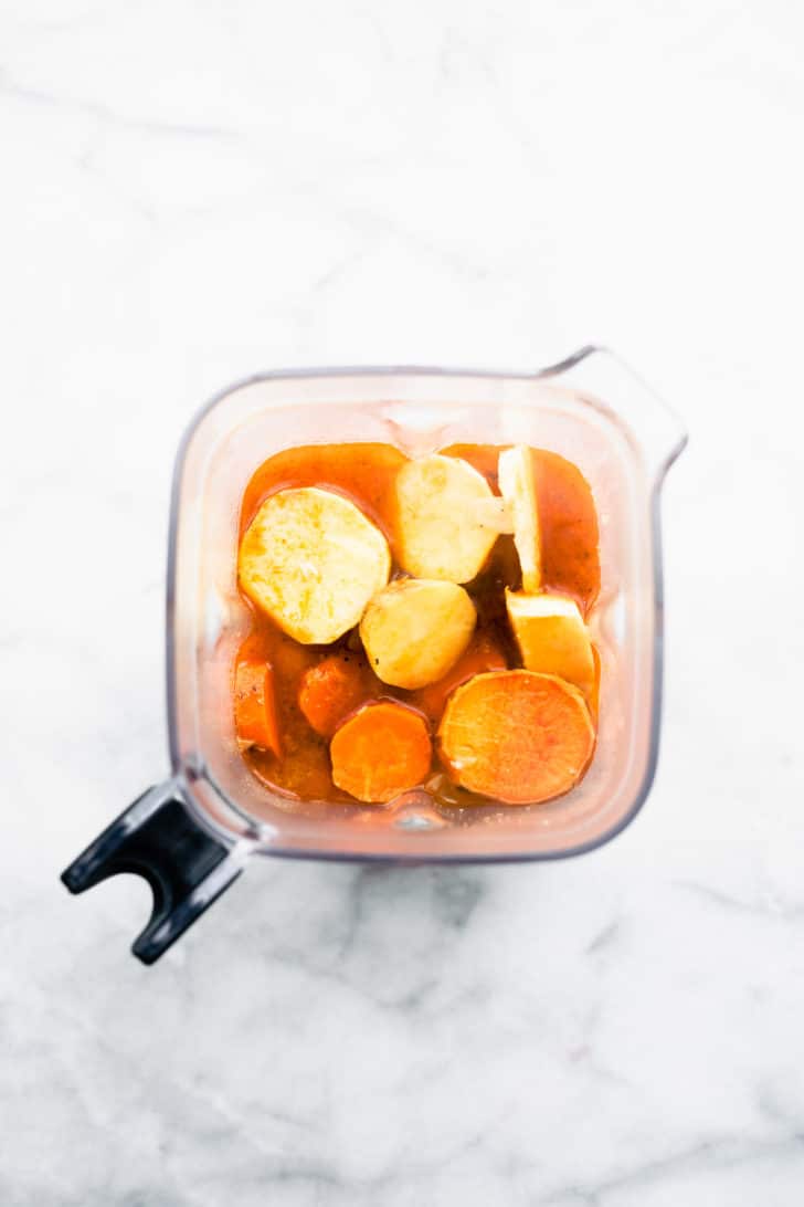 an overhead image of potatoes, parsnips, and carrots, and broth in a blender for root vegetable soup