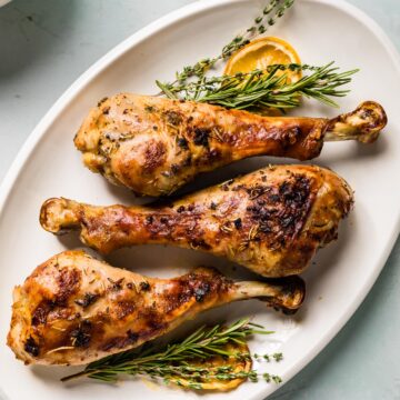 overhead photo of 3 roasted turkey legs on a platter with herbs and lemon slices