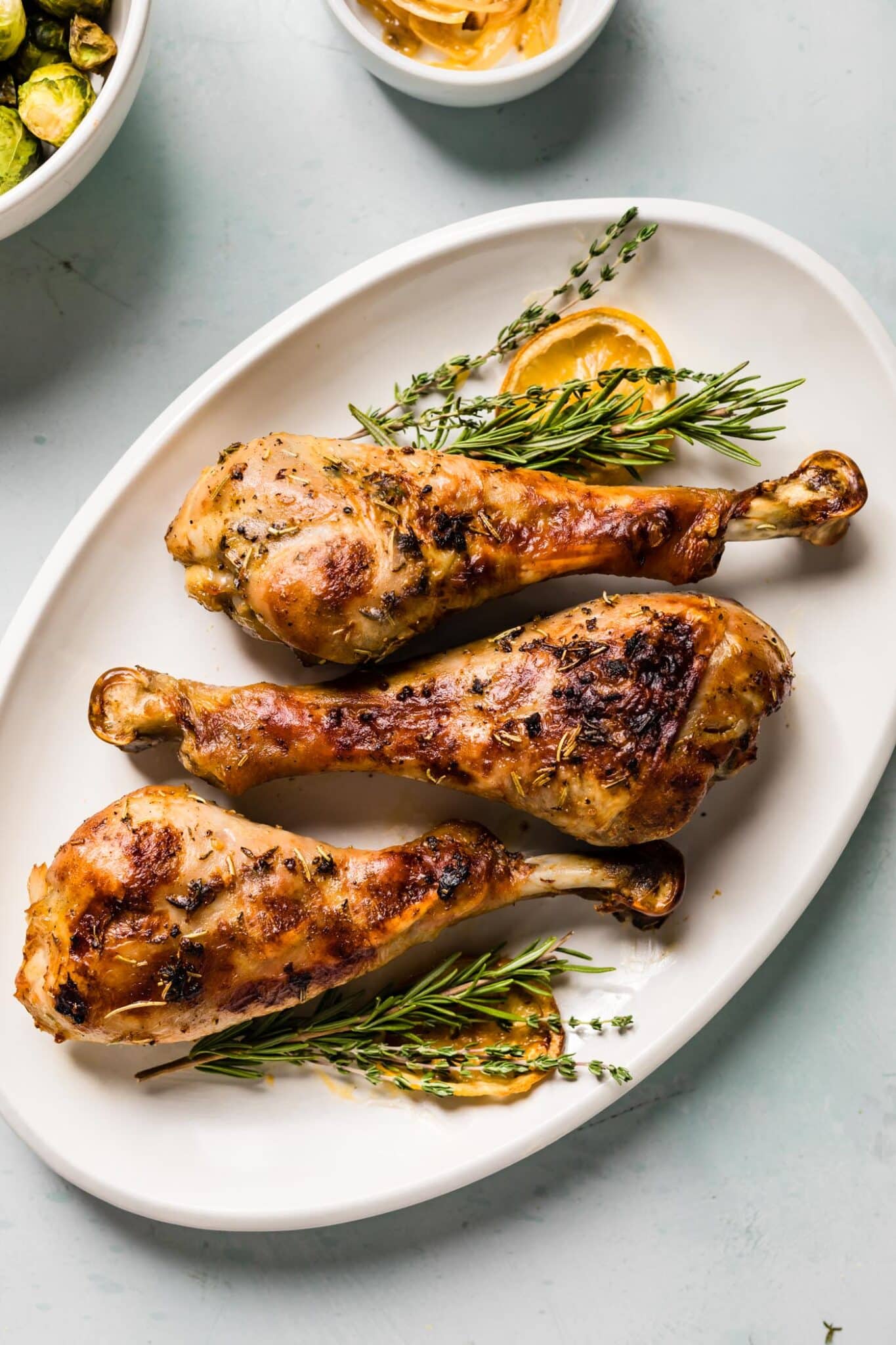 overhead photo of 3 roasted turkey legs on a platter with herbs and lemon slices