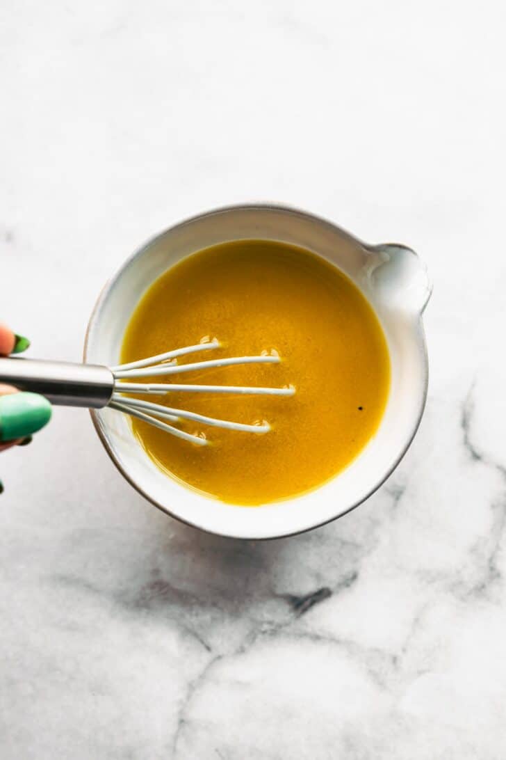 Woman's hand whisking a vinaigrette dressing in a bowl