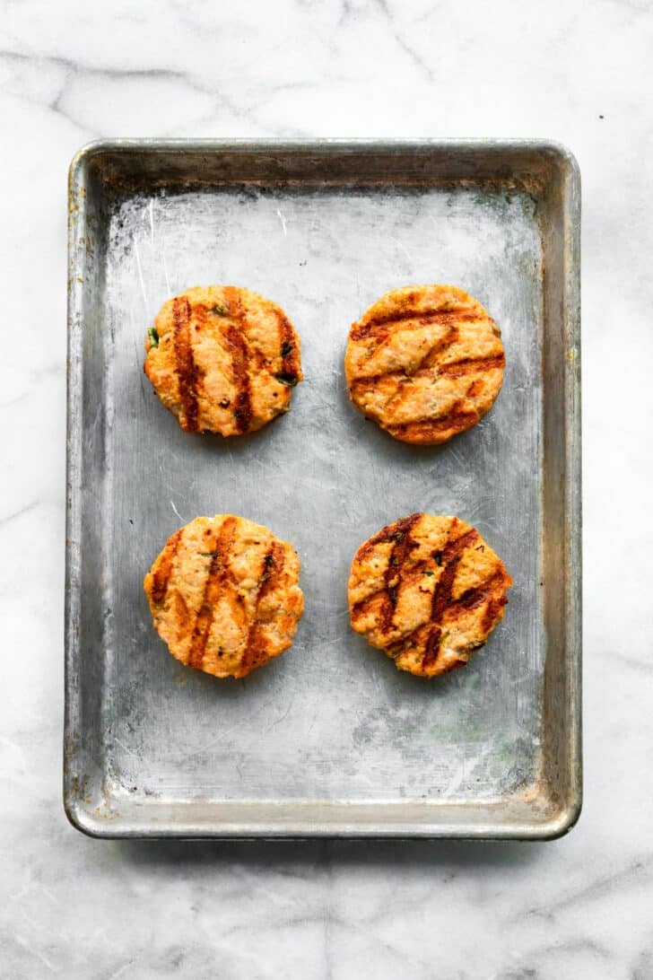 Four grilled salmon burgers on a metal sheet pan.