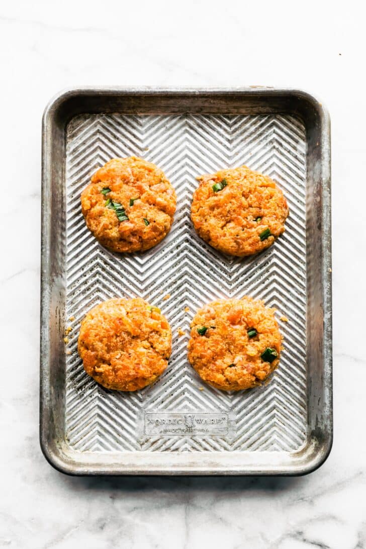 Four raw salmon burger patties on a metal sheet.