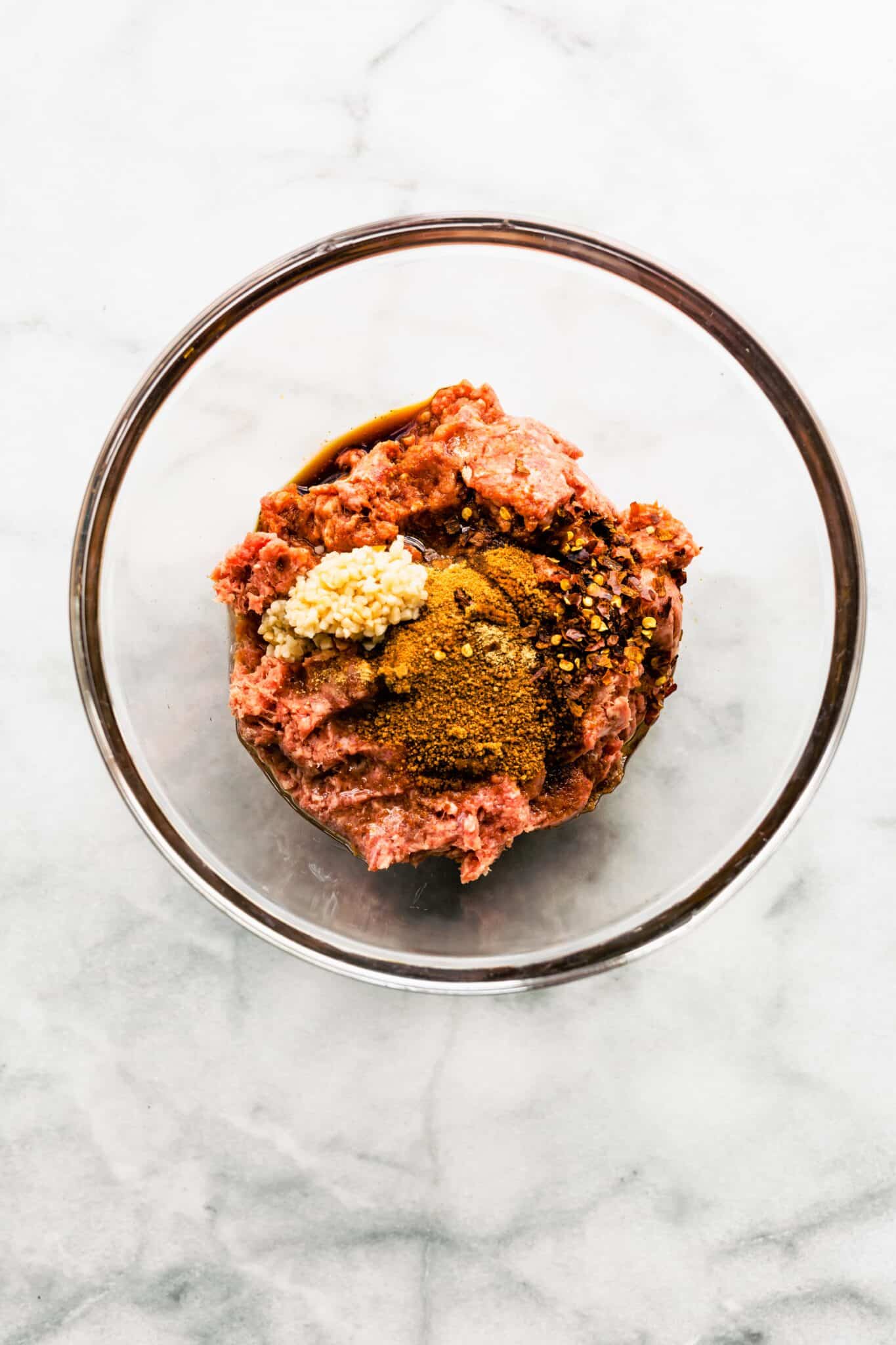 Ground beef, minced garlic and Asian spices in a glass mixing bowl.