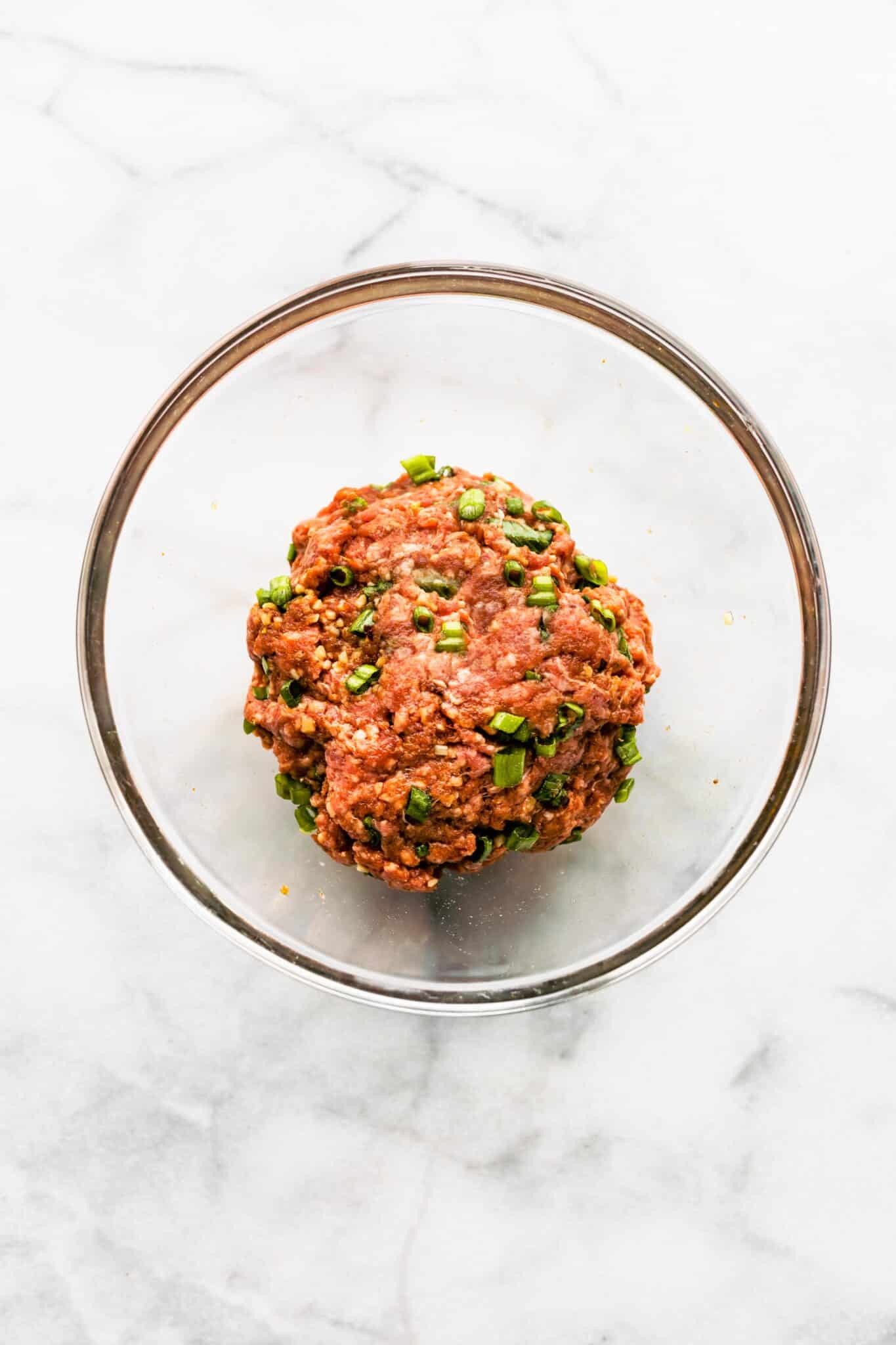 Overhead photo of ground beef mixed with green onion in a glass bowl.