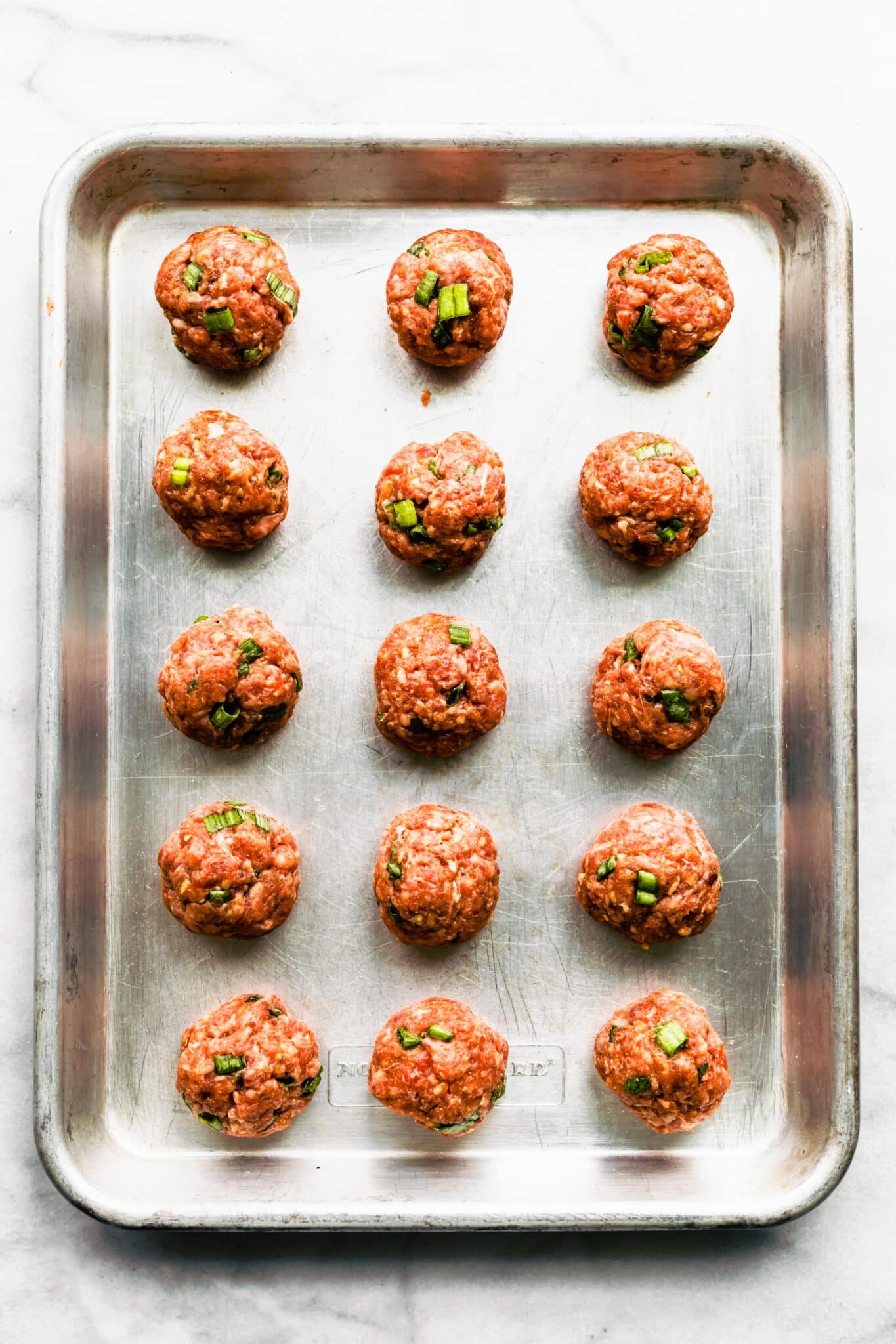 Overhead photo of fifteen raw meatballs on a baking sheet.