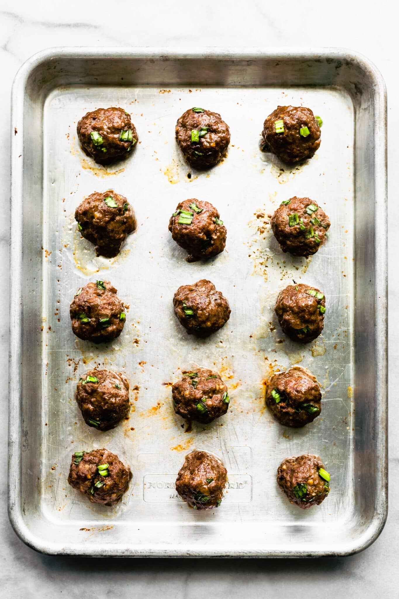 Overhead photo of fifteen baked meatballs on a metal sheet pan.