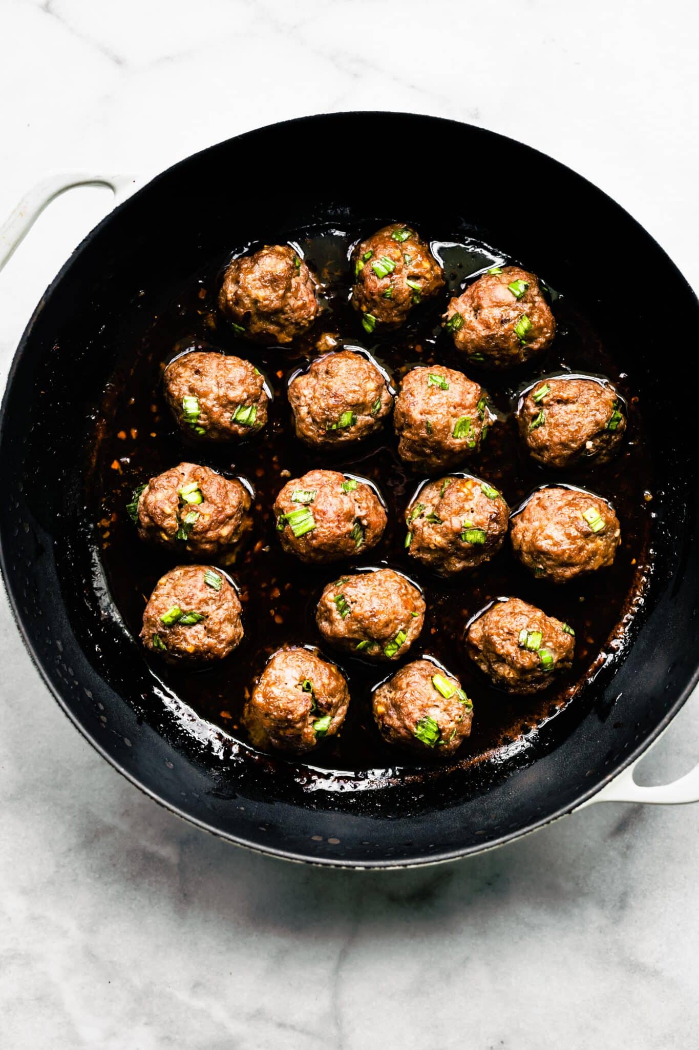 Asian meatballs on top of a sauce in a cast iron pan.
