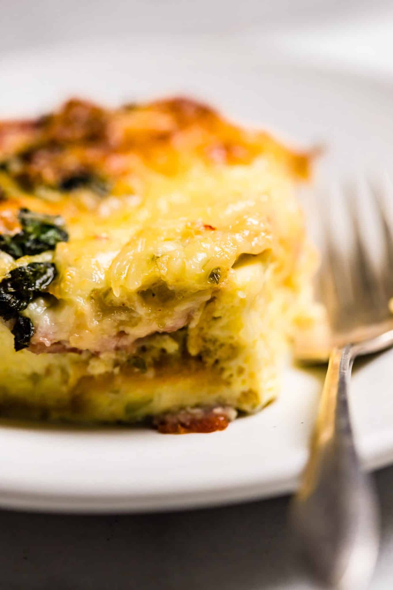 Up close shot of gluten free breakfast strata on a white plate with a fork.