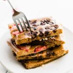 fork in stack of strawberry chocolate chip chocolate protein pancakes on white plate