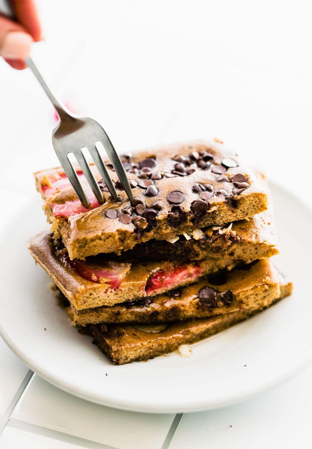 fork in stack of strawberry chocolate chip chocolate protein pancakes on white plate