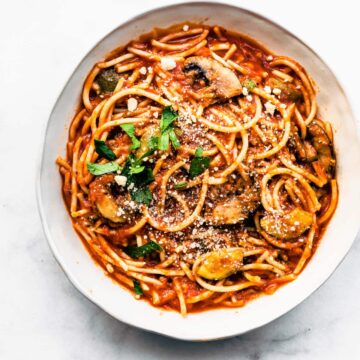 overhead image of a white bowl full of gluten free slow cooker spaghetti with mushrooms topped iwth fresh herbs
