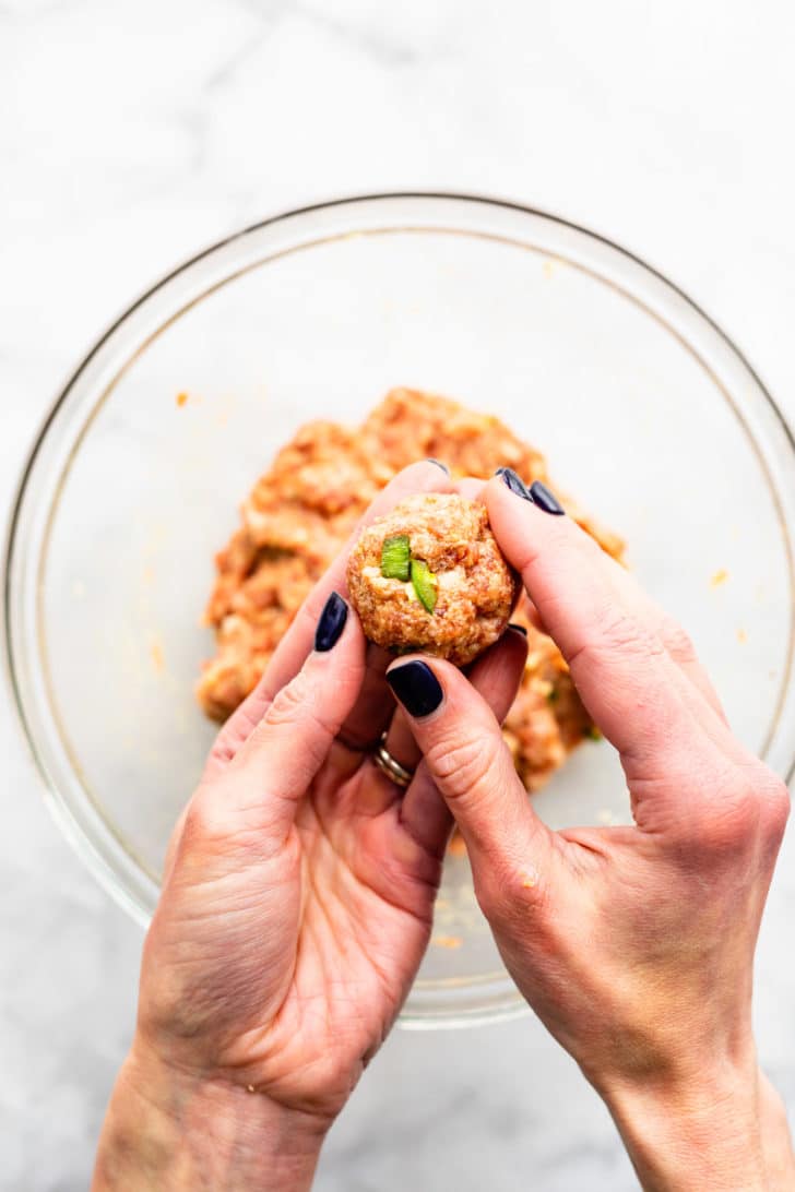 two hands rolling over a glass bowl rolling a meat mixture for gluten free meatballs with cranberry sauce