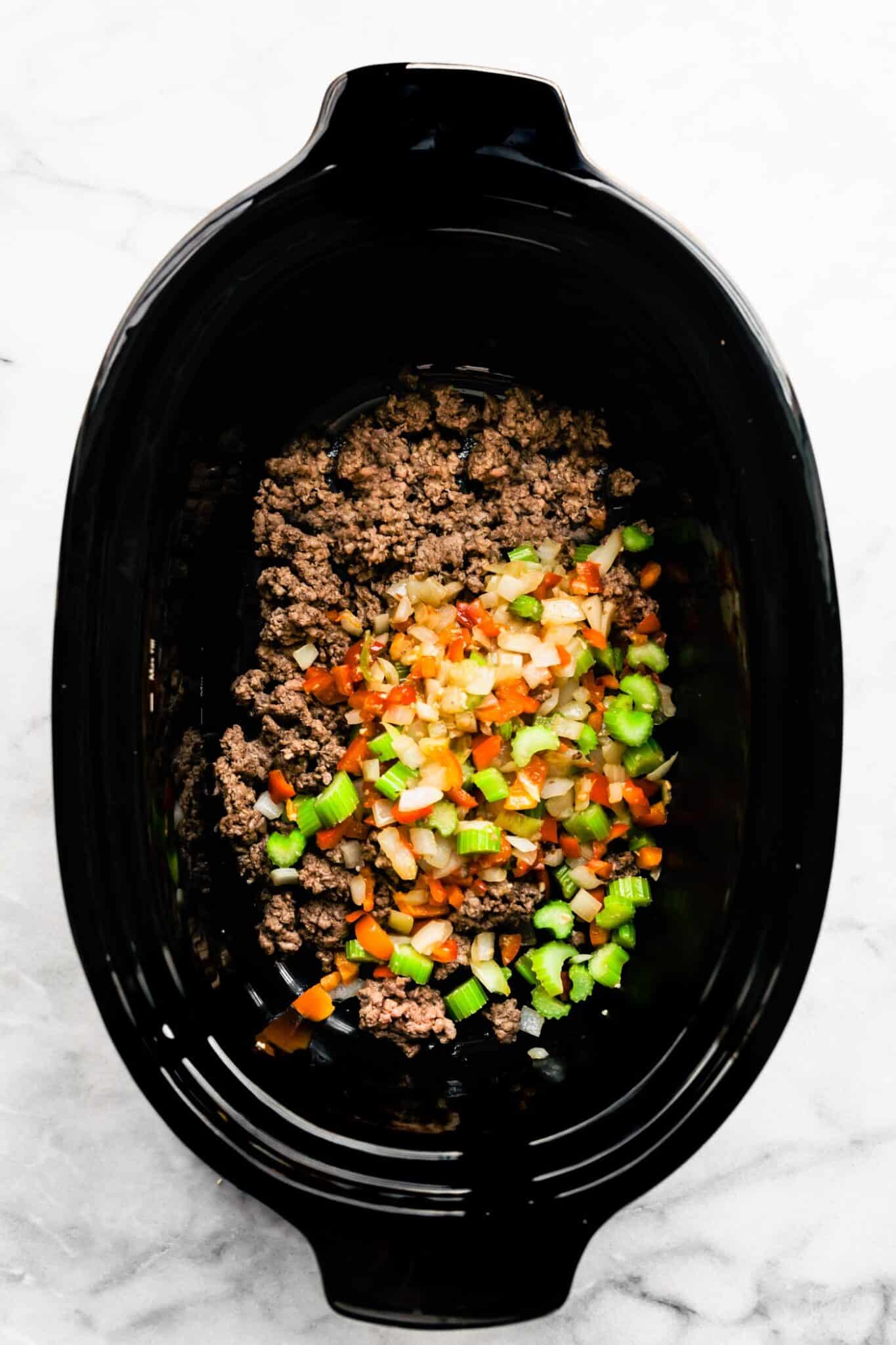 A black crockpot filled with browned ground beef and veggies.