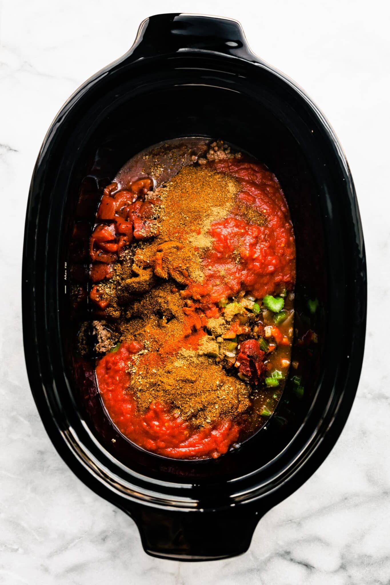 A black crockpot with crushed tomatoes, spices and ground meat.