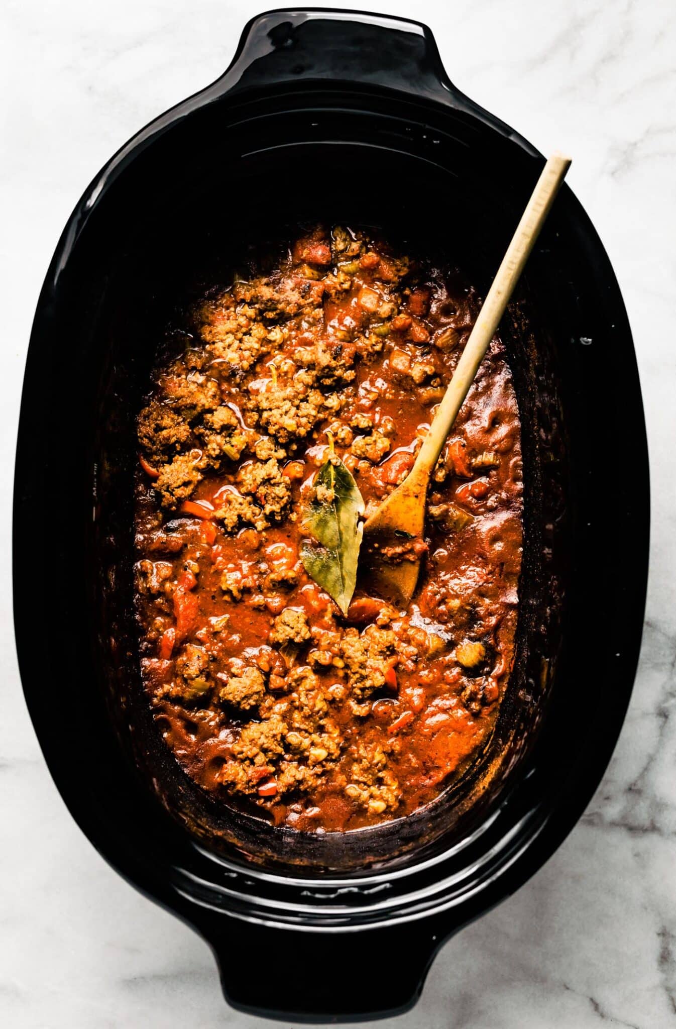 A wooden spoon and bay leaf in slow cooker beef chili.