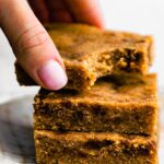 A woman's hand reaching for a stack of soft baked paleo bars on a plate.