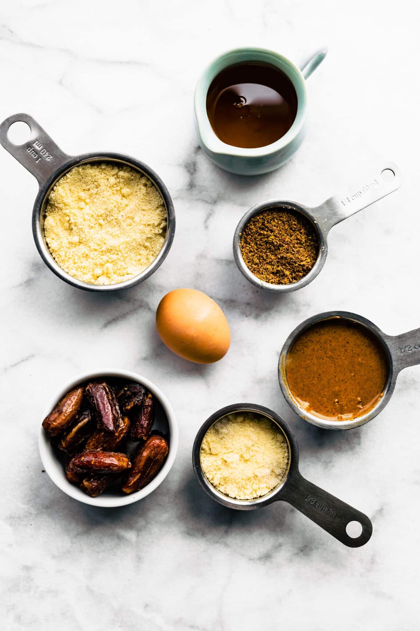 Measuring cups of ingredients for baked paleo bars like dates, almond flour and almond butter.