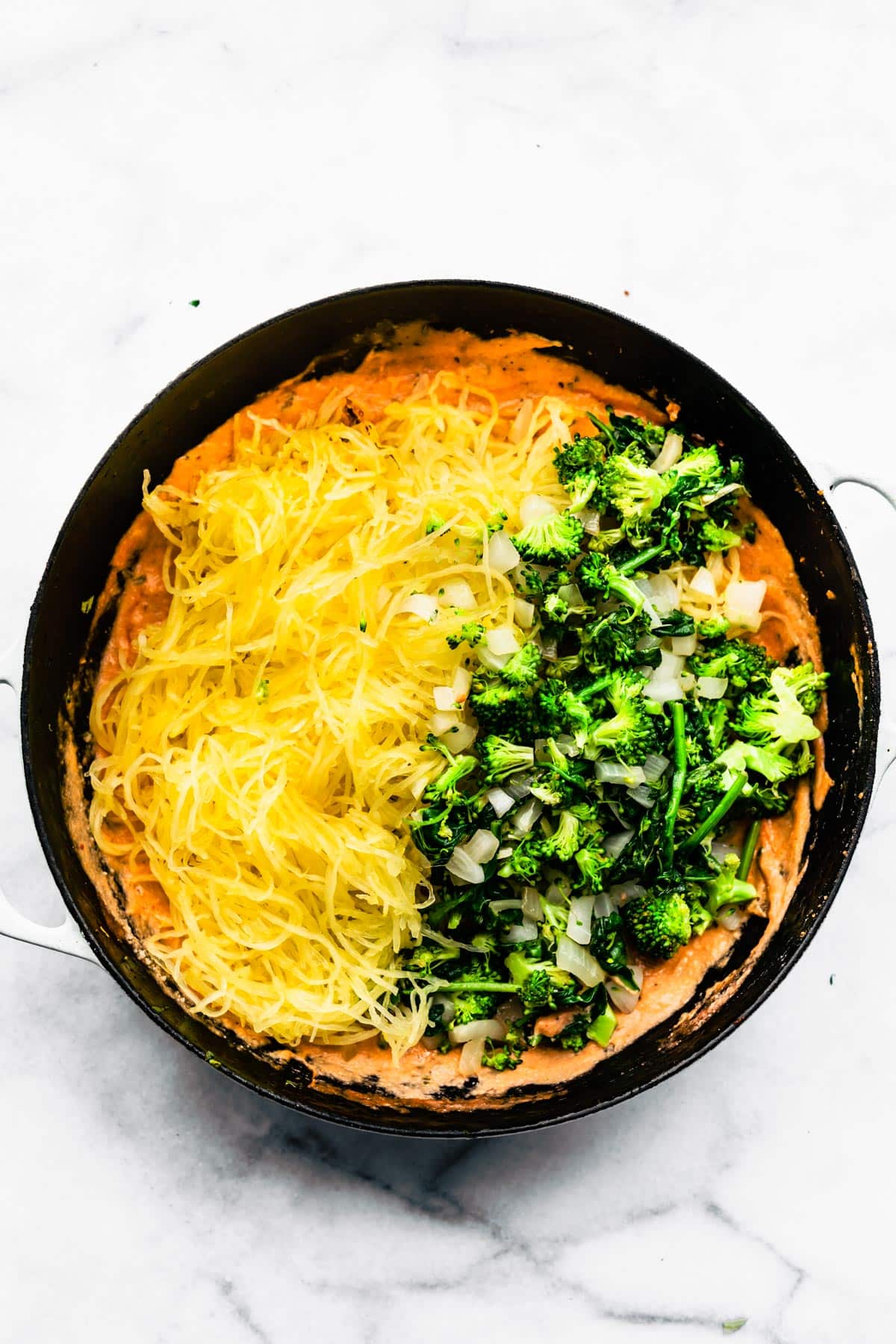 Spaghetti squash noodles and cooked veggies on a creamy marinara sauce in a pan.