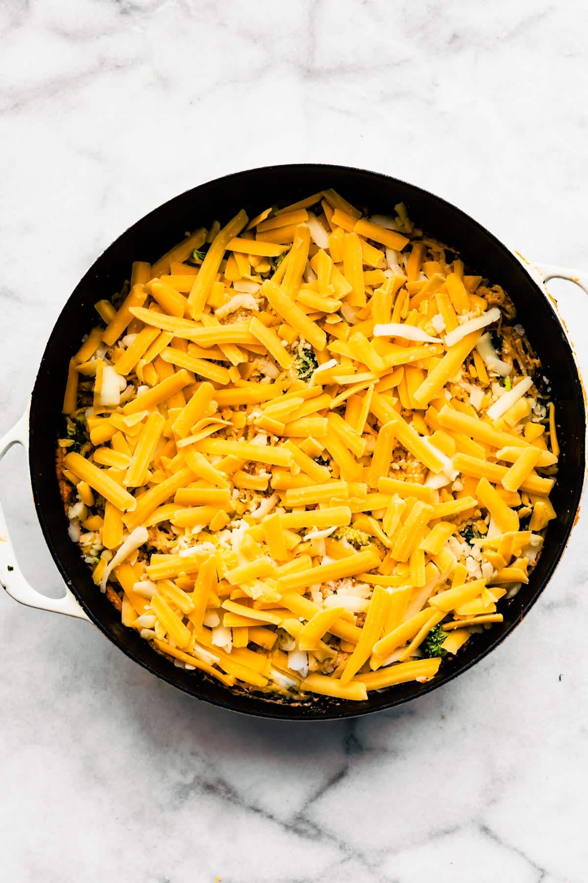 Shredded cheddar cheese on top of an uncooked spaghetti squash casserole.