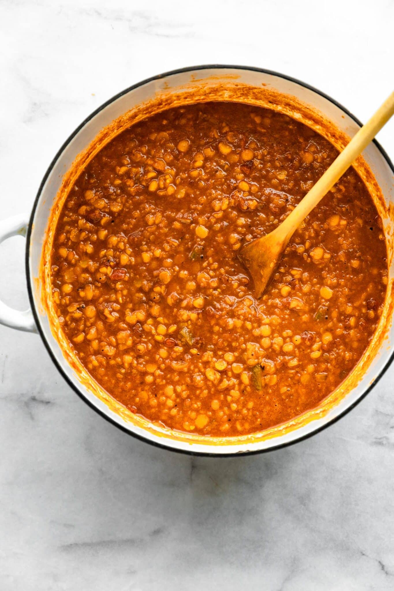 Overhead photo of a white pot filled with lentil chili and wooden spoon in it.