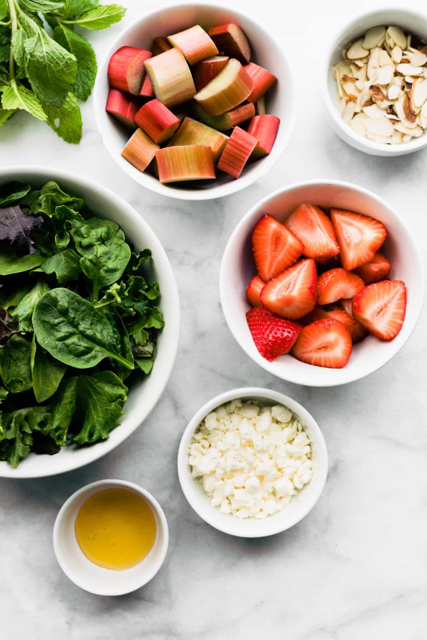 Overhead photo of bowls of spinach, rhubarb, strawberries, crumbled feta and sliced almonds.