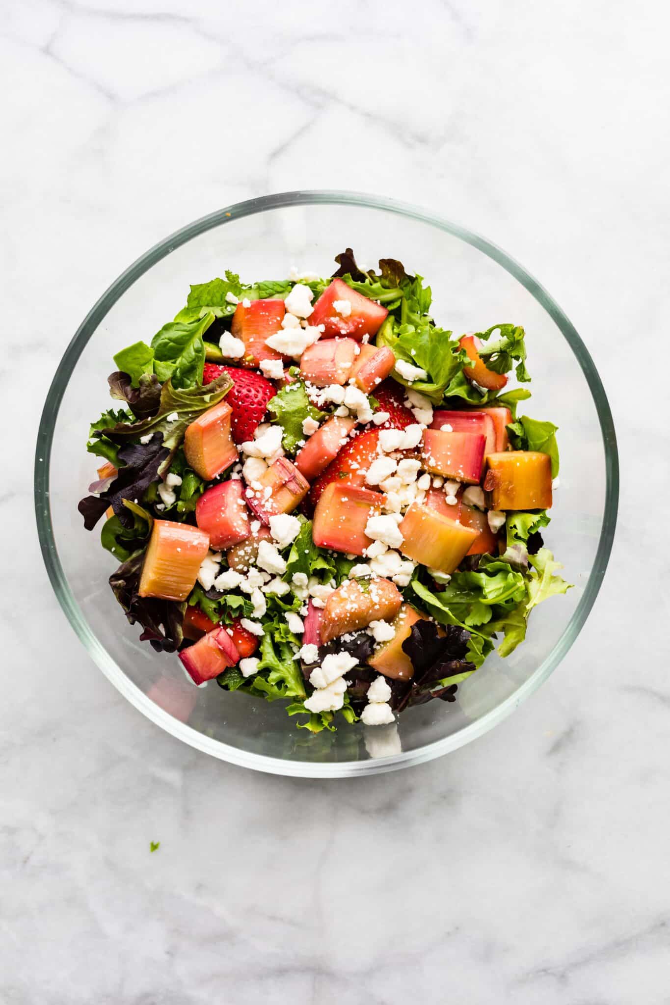 Crumbled feta cheese on a bed of mixed greens, roasted rhubarb, and strawberries.
