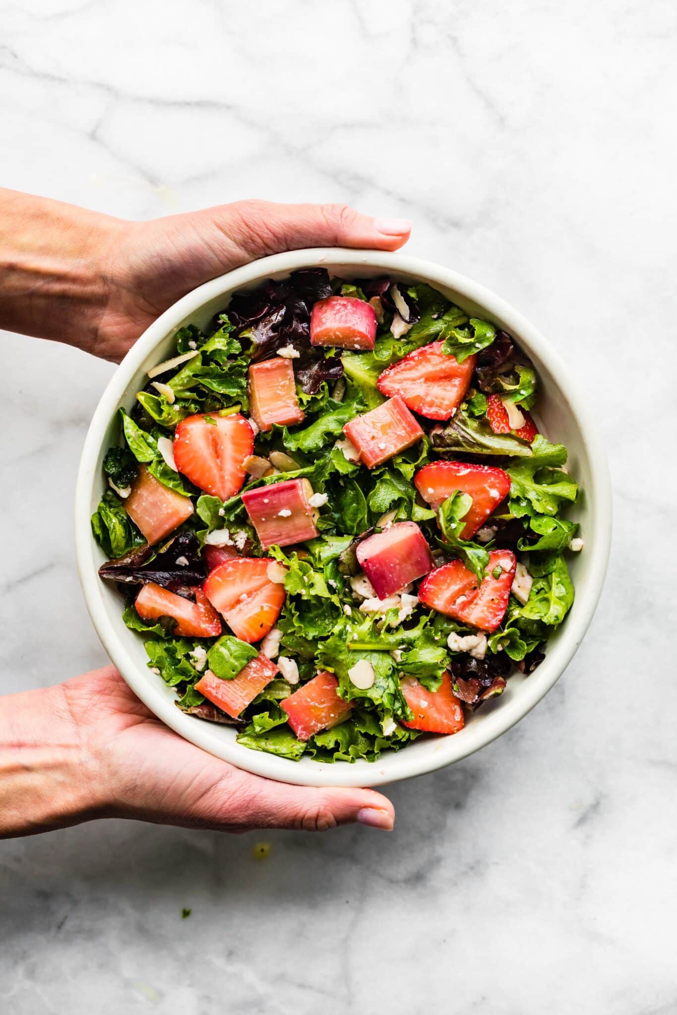 A woman's hands holding a white bowl filled with strawberry rhubarb salad.