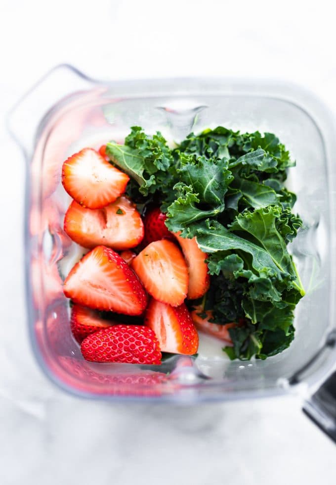Fresh sliced strawberries and softened kale inside a blender