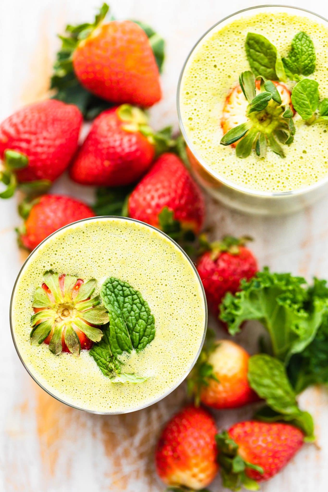 Overhead view two glasses super fruit kale smoothies in clear glasses, fresh strawberries on top and next to glasses.