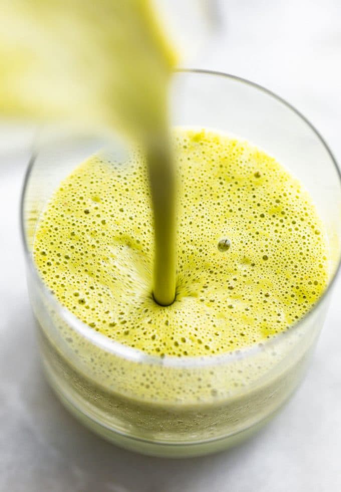 A green fruit kale smoothie being poured into a short clear glass