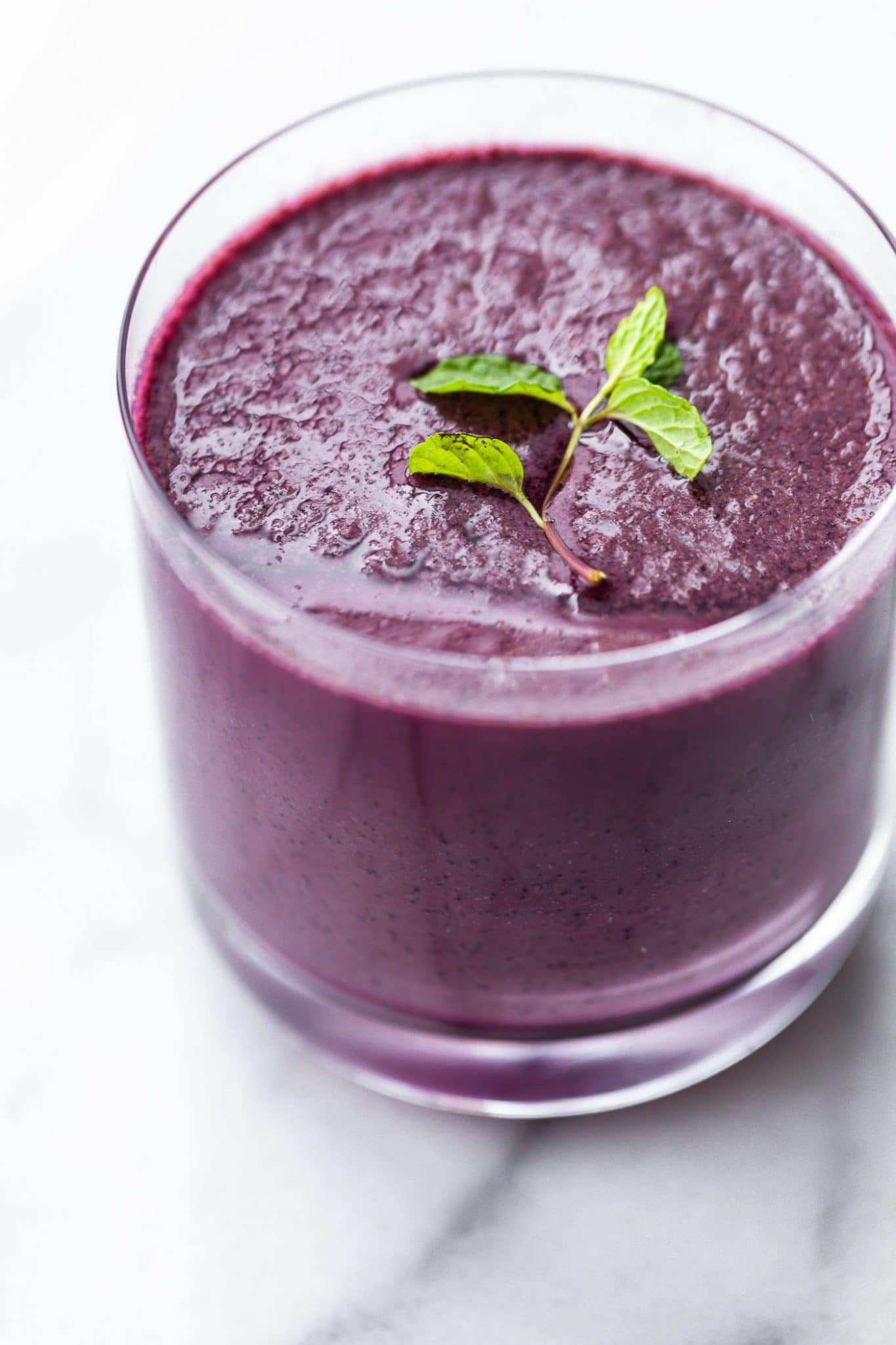 Image of a glass filled with blended berries and kale smoothie, topped with fresh mint