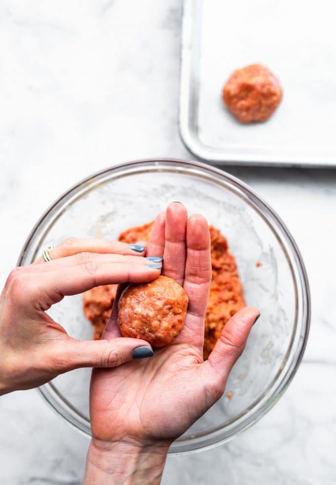 Overhead view two hands rolling out a turkey meatball for honey sriracha meatballs.