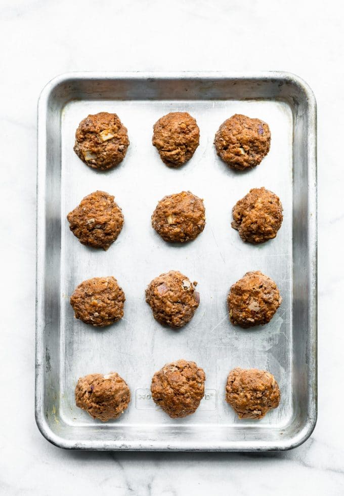 Overhead view meatballs lined up on silver baking sheet for honey sriracha meatballs.