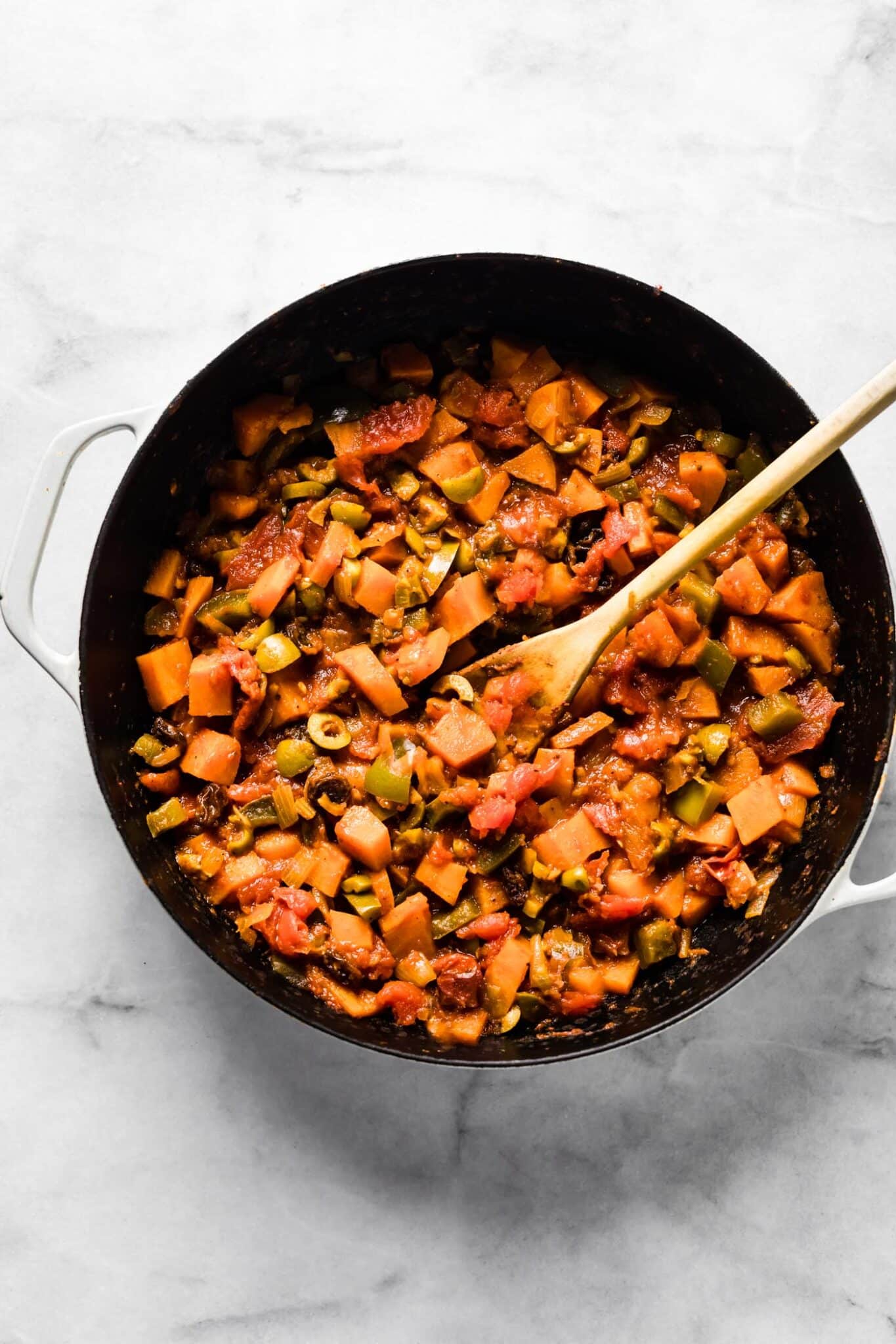A wooden spoon in a pot of vegetarian sweet potato picadillo.