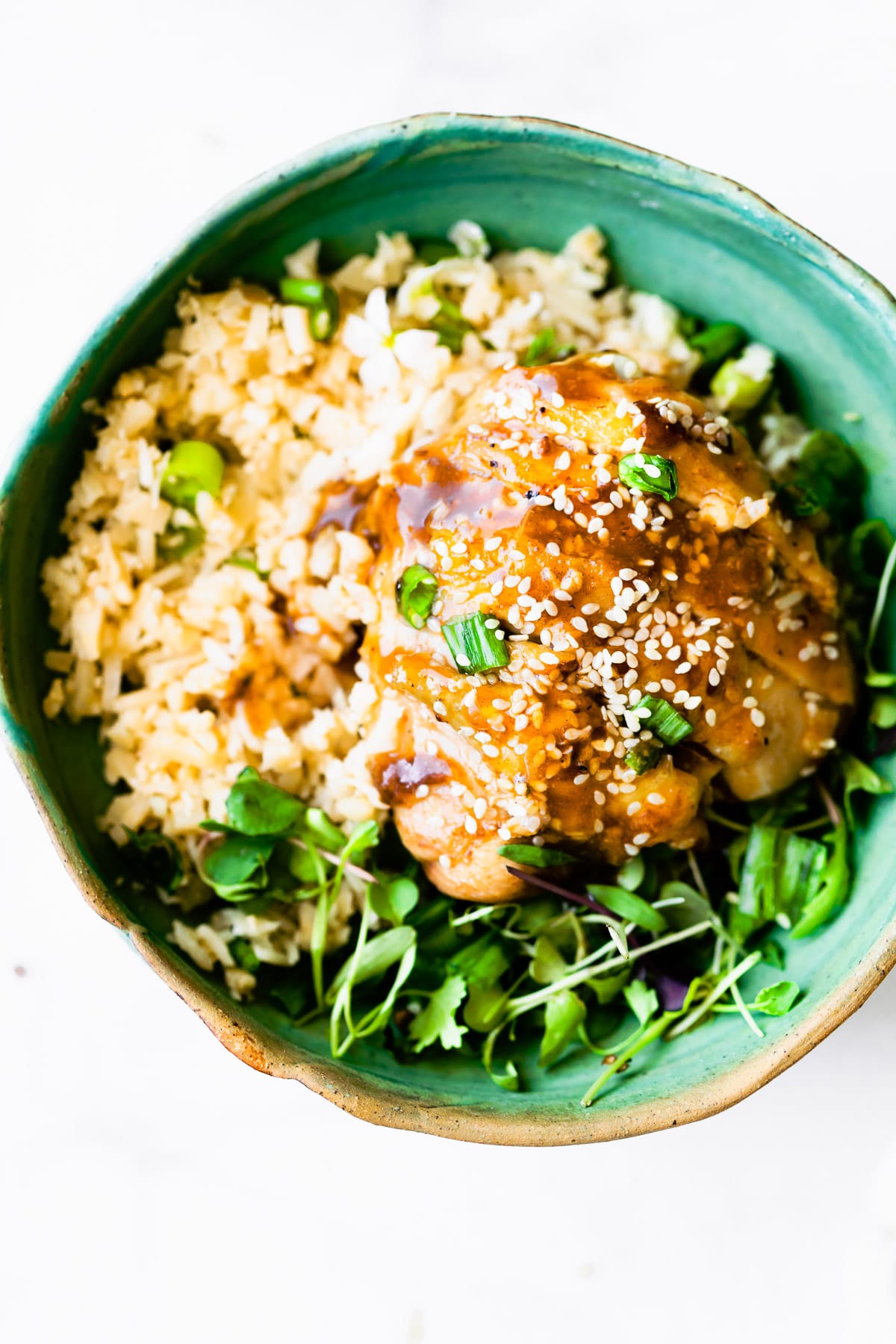 Teriyaki chicken served over bed or rice and greens in turquoise bowl