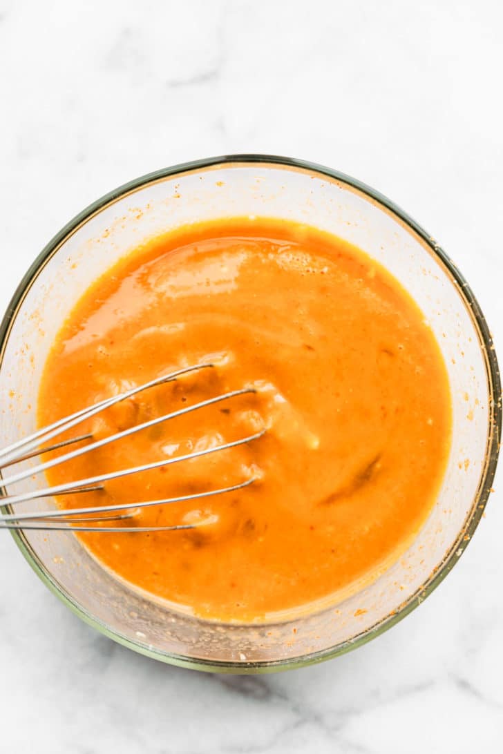 overhead image of a whisk in a glass bowl whisking eggs and an egg yolk together for tex-mex egg and cauliflower casserole
