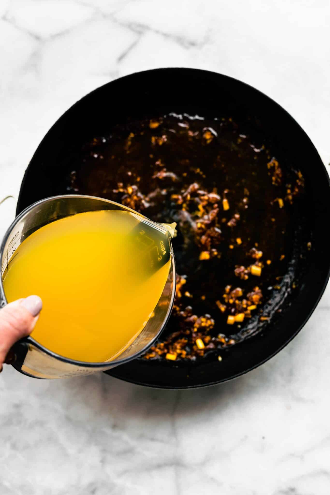 Overhead photo of broth being poured into sauteed aromatics like garlic and ginger.