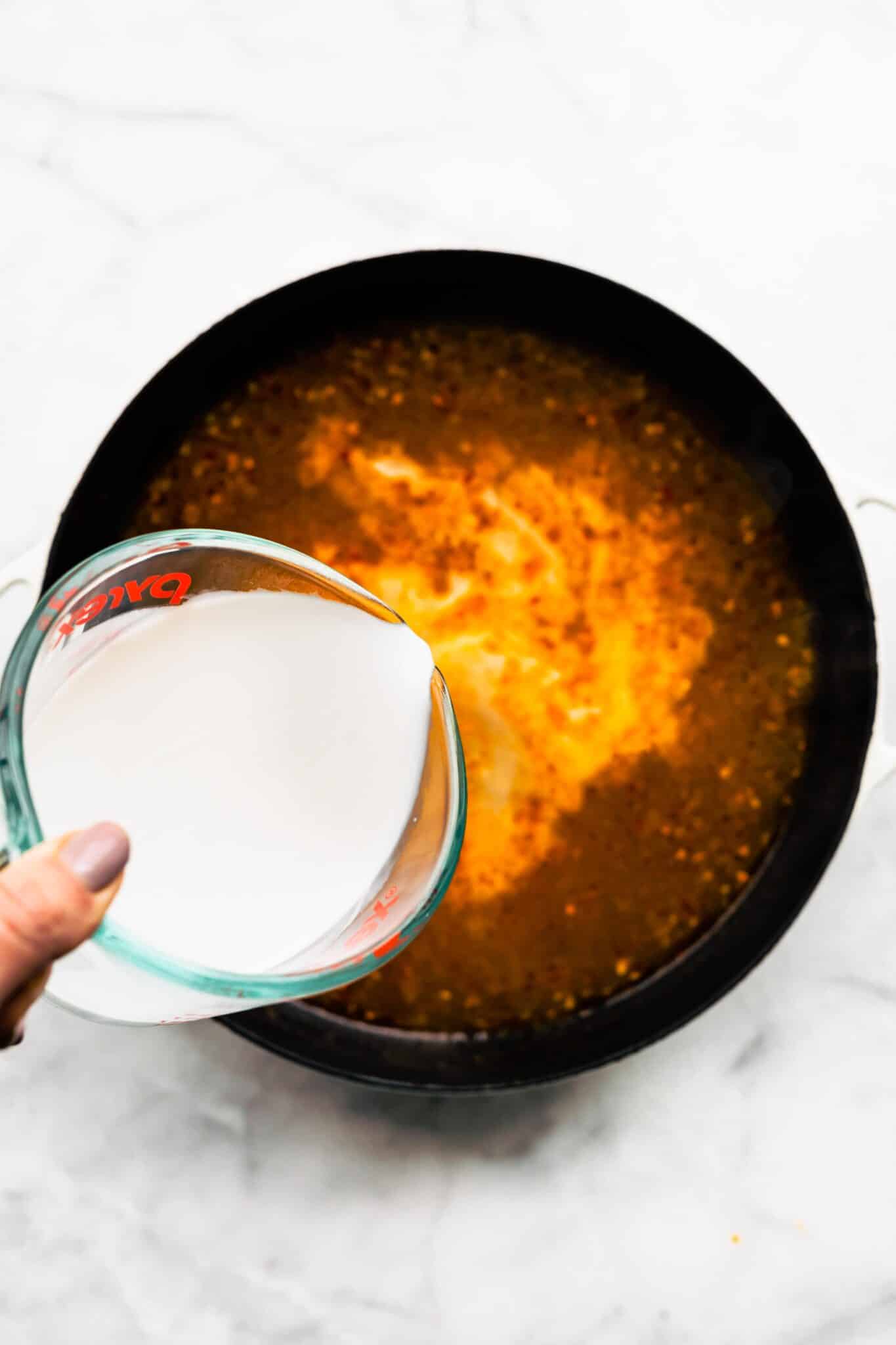 Overhead photo of a woman pouring coconut milk into a Thai Coconut Soup.
