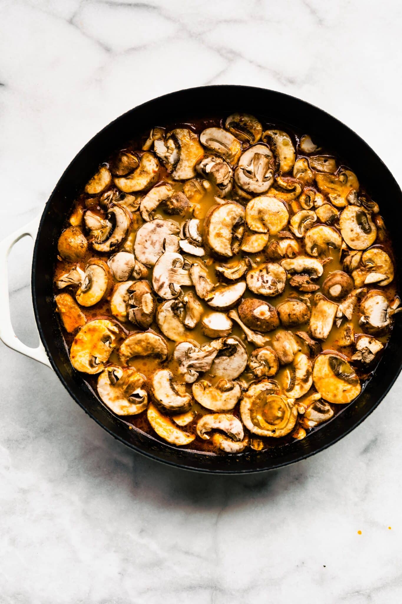 Overhead photo of sliced mushrooms in chili paste and broth in a soup pot.