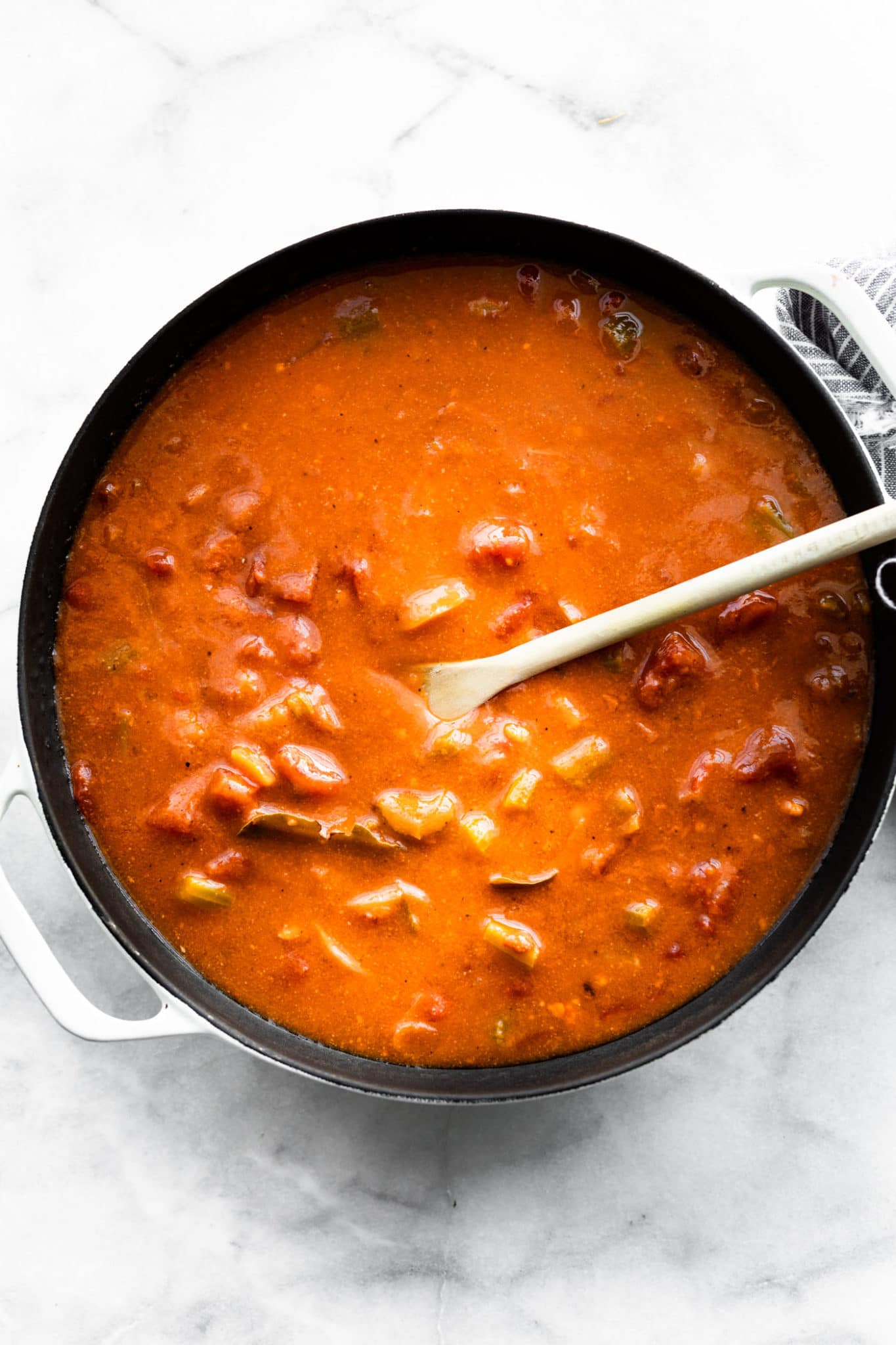a pot of tomato crab bisque being stirred with a wooden spoon