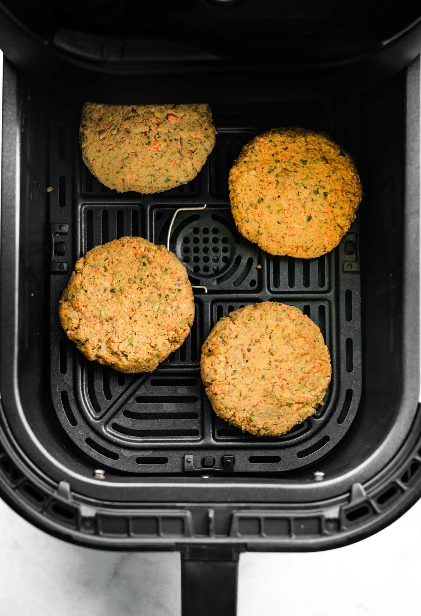 Four unbaked veggie burgers in an air fryer basket.