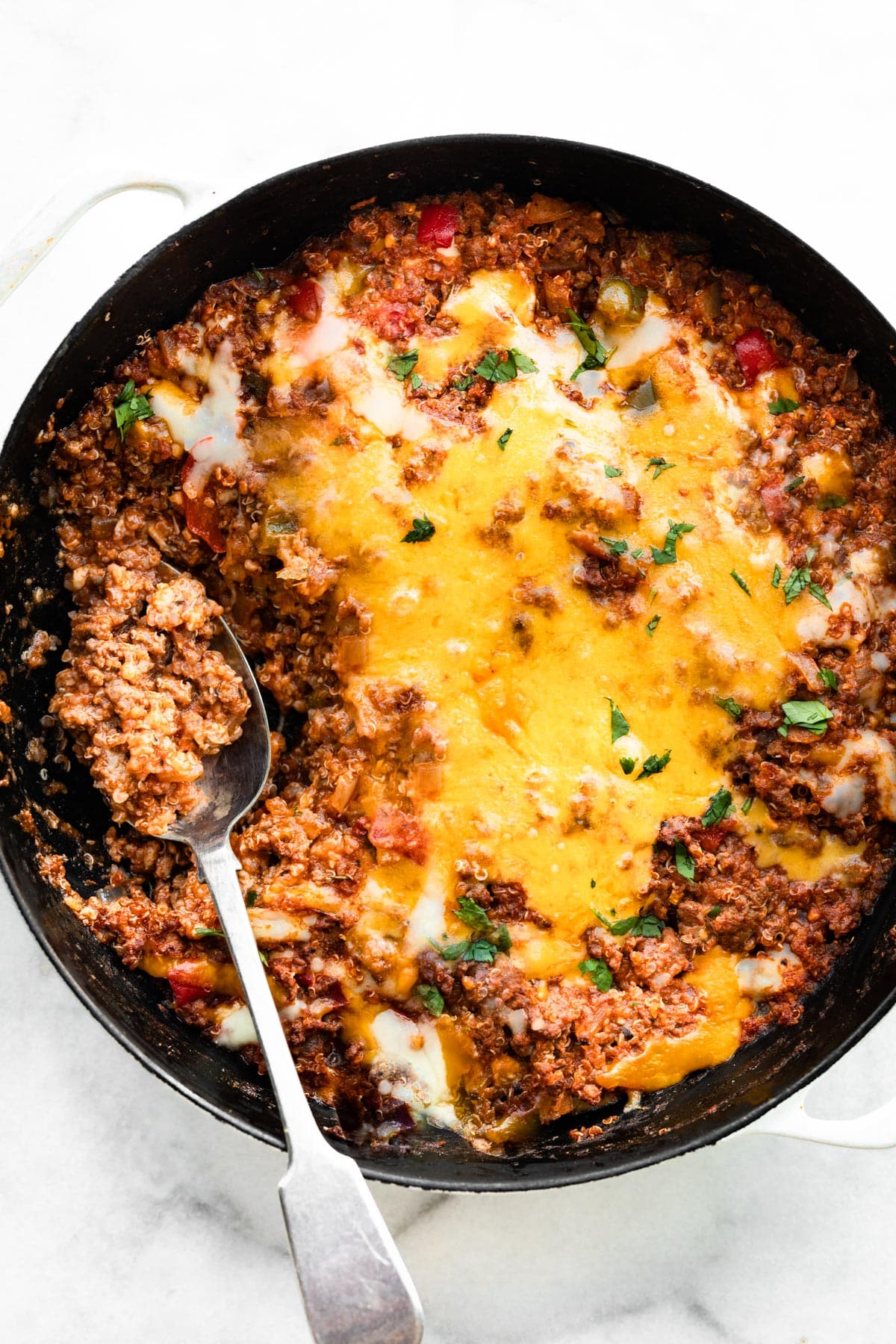 Overhead photo of a spoon in a skillet of unstuffed peppers topped with melted cheese.